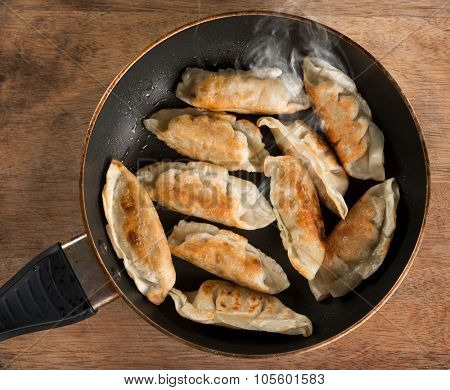 Top view close up cooking fried dumplings in a frying pan. Chinese food with hot steams, on rustic vintage wooden background. 