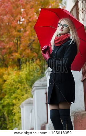 Caucasian student girl with red fully collapsible umbrella in hands and cat eye glasses posing at au