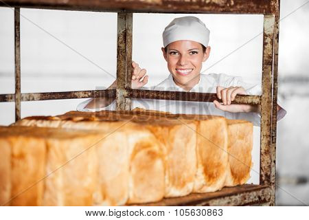 Portrait of happy female baker pushing bread rack in bakery
