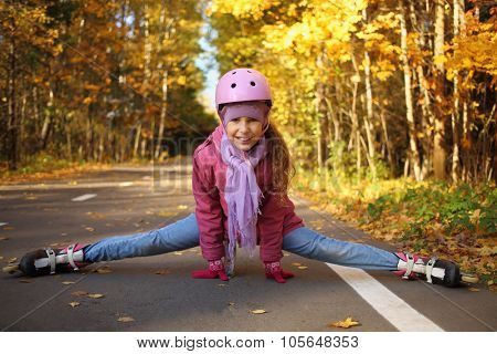 Happy girl in a protective helmet sitting on the splits in the rollers on the asphalt in the autumn park