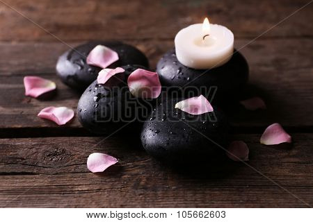 Alight candle and pebbles covered with rose petals on wooden background