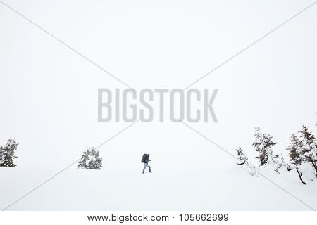 Male mountain climber with huge backpack and trekking poles having hard winter hiking trip after blizzard in Austrian Alps