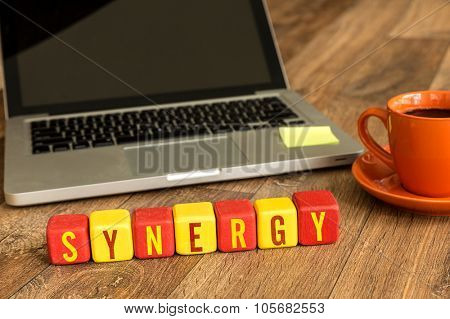 Synergy written on a wooden cube in front of a laptop