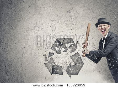 Young emotional woman crashing recycling sign with baseball bat