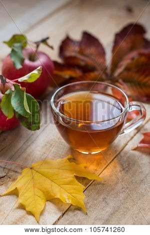 Glass Hot Cup Of Tea On A Wooden Table With Autumn Leaves And Apple