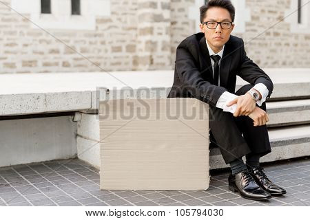 Businessman in a city street sitting next to blank banner