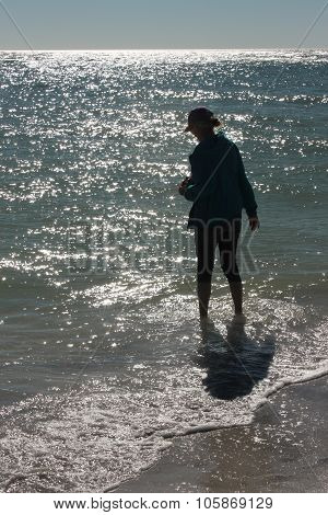 Silhouetted figure wading in sparkling ocean