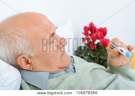 Senior gentelman checks the thermometer with a light scowl.