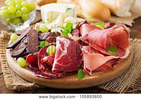 Antipasto catering platter with bacon, jerky, sausage, blue cheese and grapes on a wooden background