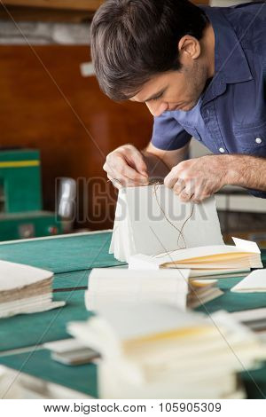 Mid adult male worker binding book at table in paper factory