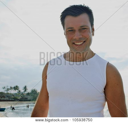 young brunette man on beach at sea smiling, gomosexual in white dress big muscles