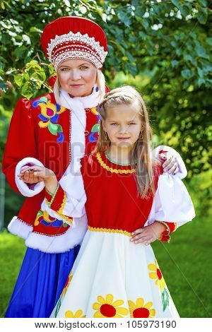 Portrait of mother and daughter in a national Russian costume on a background of green summer park