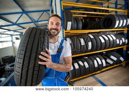 smiling auto mechanic carrying tire in tire store