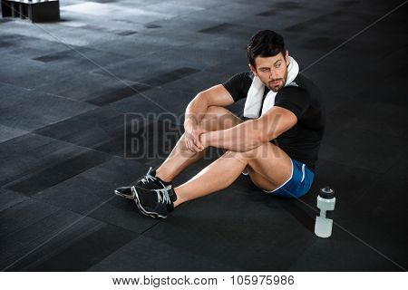 Sportsman wearing blue shorts and black t-shirt sitting on the floor in gym