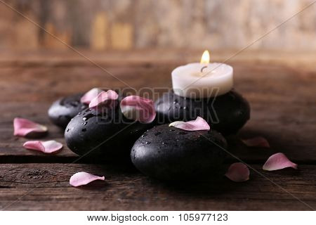Alight candle and pebbles covered with rose petals on wooden background