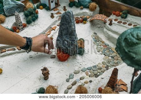 Sand therapy. Man arranges with his hand toy miniature trees and small houses in a sand box. Anti-stress psychological rehabilitation therapy
