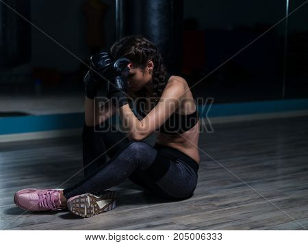 Upset young fighter boxer girl wearing boxing gloves siting on the floor after loosing fight