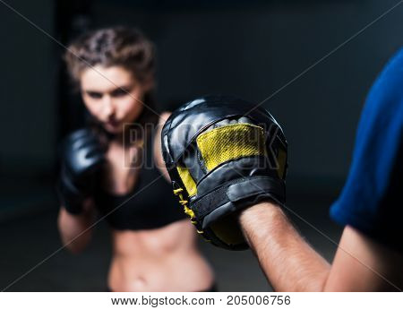 Young fighter boxer fit girl wearing boxing gloves in training  with  personal trainerin gym. Low key selective focus image. Woman power