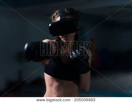 Young fighter boxer fit girl in VR glasses wearing boxing gloves in training. Boxing game in virtual reality 360 degrees. Futuristic gaming