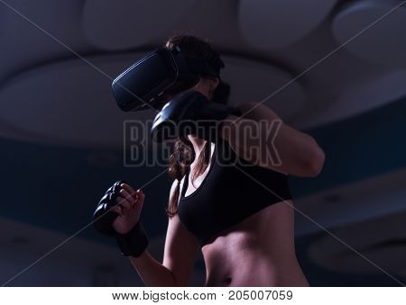 Young fighter boxer fit girl in VR glasses wearing boxing gloves in training. Boxing game in virtual reality 360 degrees. Futuristic gaming