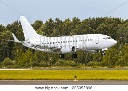The airplane is landing on the runway at airport against the background of the forest and blue sky. Summer sunny weather