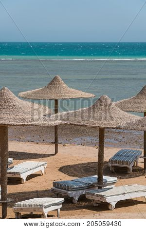 A view of the red sea in Egypt with wicker peaks from umbrellas in the foreground.