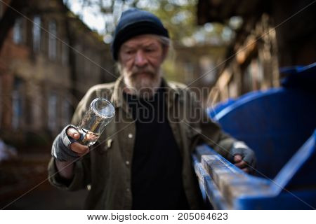 Dirty old tramp looking at empty bottle in his hand. Difficult life of homeless old man.