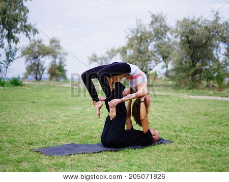 Beautiful woman and girl practise yoga pose outside. Women doing stretching workout in park outdoors at sunset.