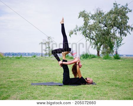 Beautiful woman and girl practise yoga pose outside. Women doing stretching workout in park outdoors at sunset.