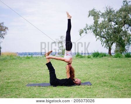 Beautiful woman and girl practise yoga pose outside. Women doing stretching workout in park outdoors at sunset.