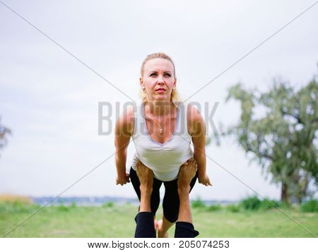 Girl in white shirt exercises yoga outdoor, on green grass.