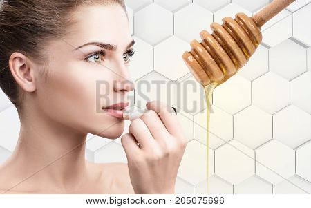 Young woman putting organic lipbalm with honey on lips over gray honeycombs background.
