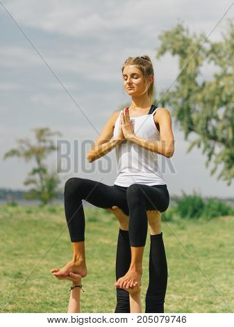 Girl in white shirt exercises yoga outdoor, on green grass.