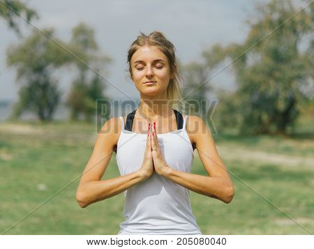 Girl in white shirt exercises yoga outdoor, on green grass.