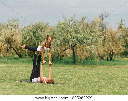 Girl in white shirt exercises yoga outdoor, on green grass. Blue sky on the background.