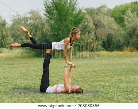 Girl in white shirt exercises yoga outdoor, on green grass. Blue sky on the background.