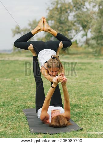 Girl in white shirt exercises yoga outdoor, on green grass. Blue sky on the background.