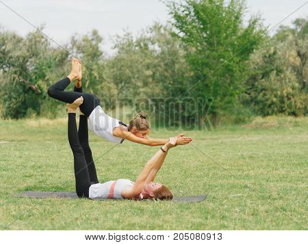 Girl in white shirt exercises yoga outdoor, on green grass. Blue sky on the background.