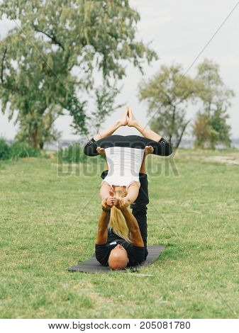 Girl in white shirt exercises yoga outdoor, on green grass. Blue sky on the background.