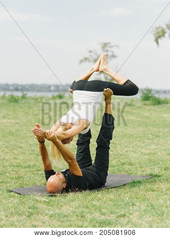 Girl in white shirt exercises yoga outdoor, on green grass. Blue sky on the background.
