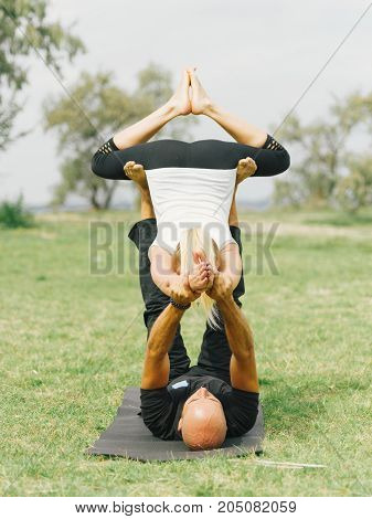 Girl in white shirt exercises yoga outdoor, on green grass. Blue sky on the background.