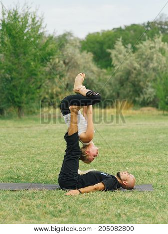 Women doing stretching workout in park outdoors at sunset. Beautiful woman and man practise yoga pose outside.