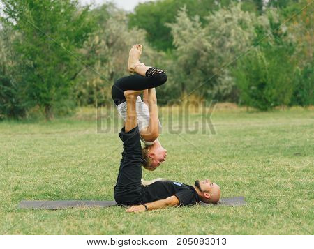 Women doing stretching workout in park outdoors at sunset. Beautiful woman and man practise yoga pose outside.