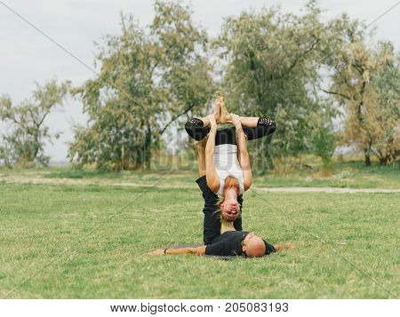 Women doing stretching workout in park outdoors at sunset. Beautiful woman and man practise yoga pose outside.