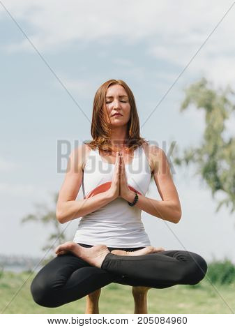 Girl in white shirt exercises yoga outdoor, on green grass.