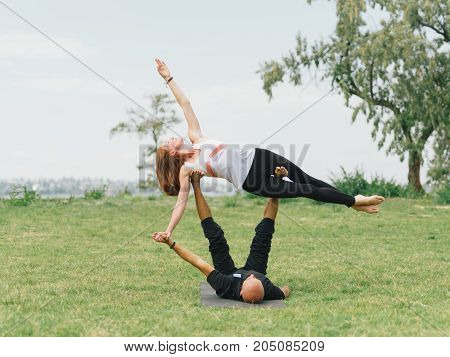 Women doing stretching workout in park outdoors at sunset. Beautiful woman and man practise yoga pose outside.
