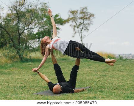 Women doing stretching workout in park outdoors at sunset. Beautiful woman and man practise yoga pose outside.