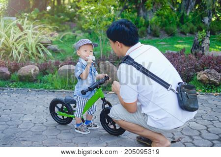 Father spend time with Cute little Asian 18 months / 1 year old toddler boy child Dad and son play and have fun with balance bike (run bike) Dad tech son to ride bike while kid smell the flower