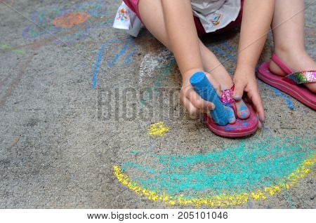 Little girl paints her toe nails blue with the help of some sidewalk chalk showiing creativity and thinking outside the box.