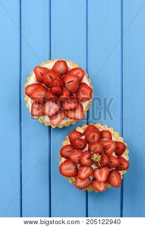 Two tasty tartlets carefully decorated with fresh strawberries on bright blue background copyspace above view